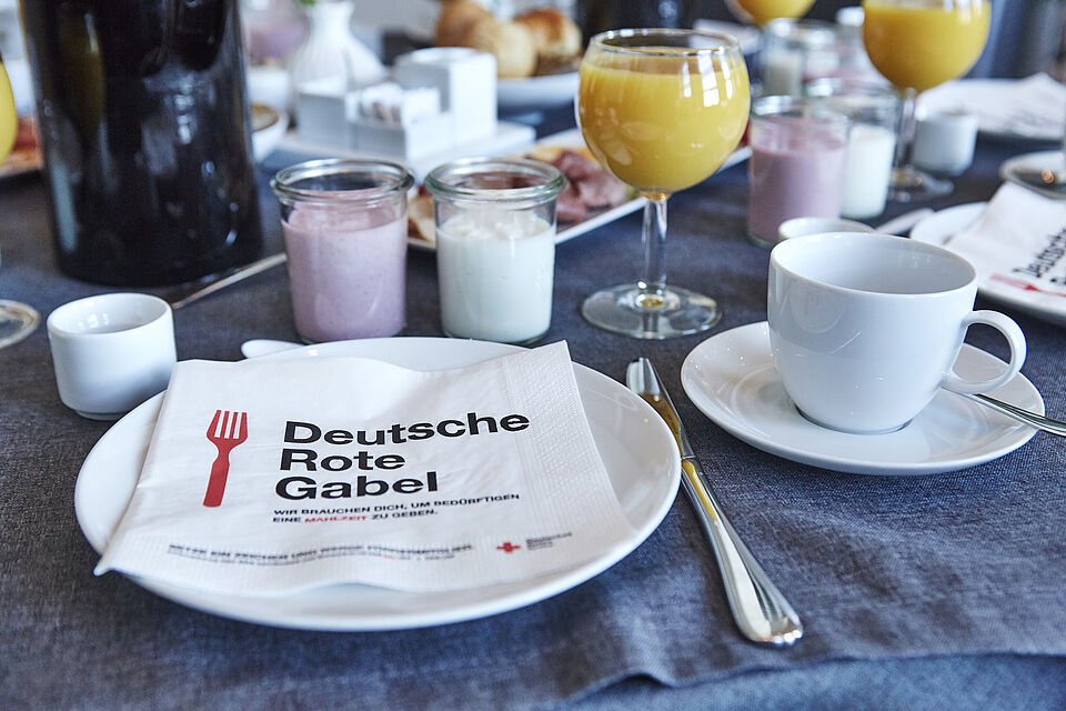 Blick auf einen reich gedeckten Frückstückstisch. Auf dem Teller liegt eine Serviette mit dem Kampagnenlogo Deutsche Rote Gabel.